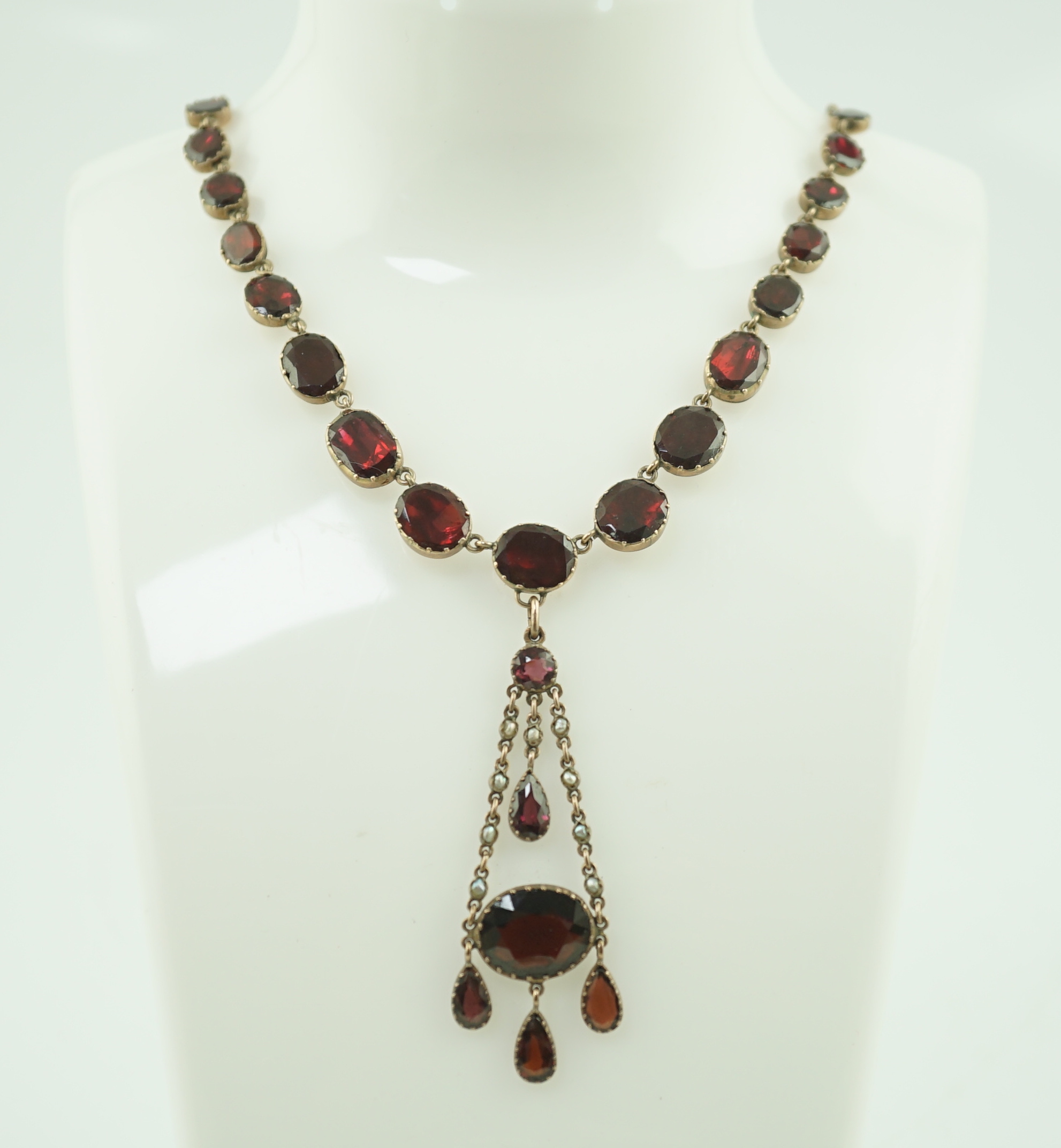 An early 19th century gold, and thirty five graduated foil backed garnet set necklace, with later garnet and seed pearl set drop